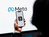 Una mano sostiene un smartphone frente a un gran logotipo de Meta