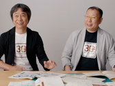 Una captura de pantalla de Shigru Miyamoto y Tezuka Takashi con camisetas del 30º aniversario de Super Mario Bros