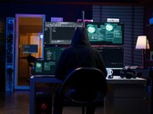 Figura encapuchada en un montaje multipantalla ejecutando un ciberataque.