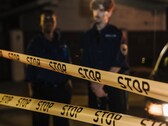 Dos agentes de policía de pie por la noche detrás de una cinta amarilla que dice Stop