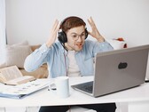Hombre con auriculares levantando las manos con frustración frente a un portátil