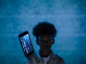 Smartphone flotante con código en la pantalla frente a un fondo azul, con una persona desenfocada detrás