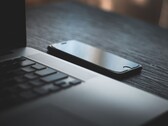 Un smartphone junto a un ordenador portátil abierto sobre un escritorio oscuro