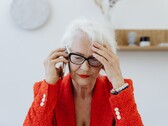 Una mujer mayor, de pelo blanco y con gafas, hablando por teléfono en un salón luminoso, con la mano apoyada en la sien.